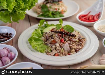Deep-fried mackerel topped with galangal, pepper, mint, red onions in a white dish with a variety of vegetables.