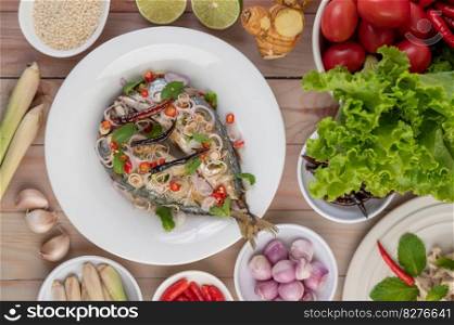 Deep-fried mackerel topped with galangal, pepper, mint, red onions in a white dish with a variety of vegetables.