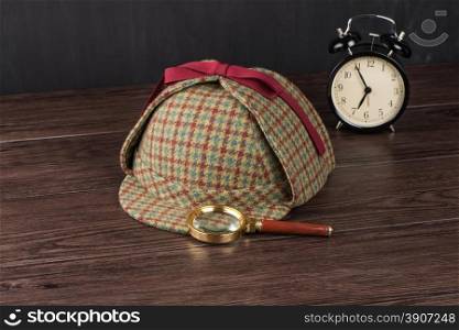 Deerstalker or Sherlock Hat and magnifying glass on Old Wooden table.