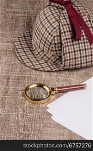 Deerstalker or Sherlock Hat and magnifying glass on Old Wooden table.
