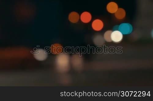 Defcoused shot of traffic at night with cars and people passing by. Blurred city lights