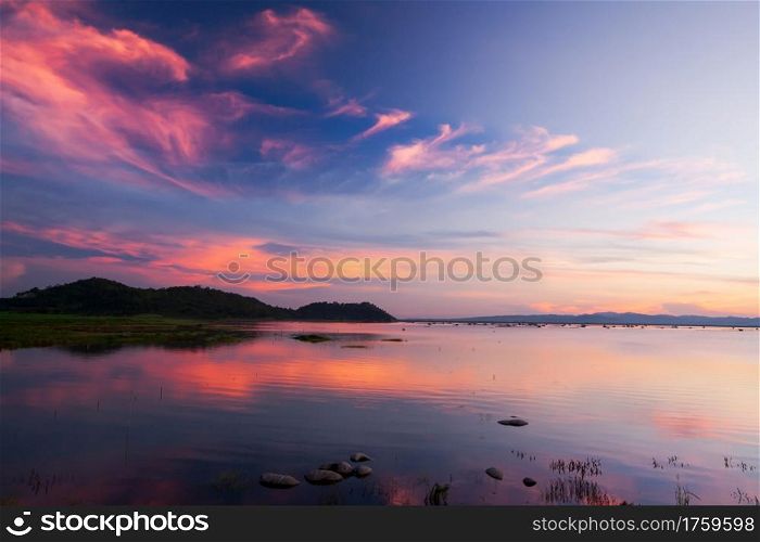 Defocus. Beautiful twilight sky above a tropical lake, gently light pink clouds against the blue sky at dusk, soft reflection of clouds on surface of freshwater, rural scene in West Thailand.