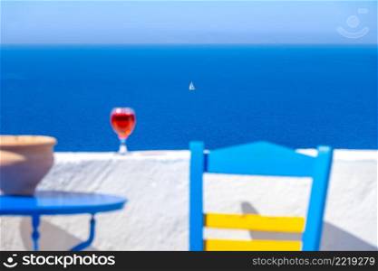 Defocused chair, table and glass of wine and a white sailing yacht far into the sea. Glass of Wine and Sailing Yacht far Into the Sea