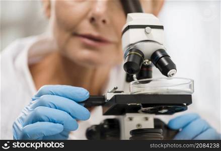 defocused female scientist looking through microscope