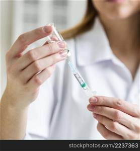 defocused female scientist with safety glasses holding syringe with vaccine