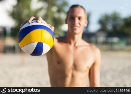 defocused shirtless male volleyball player beach holding ball