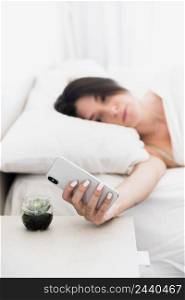 defocussed young woman lying bed looking smartphone