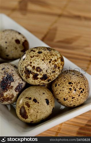 Delicate, beautiful Quail Eggs in a white bowl on a bamboo mat. Shallow dof.