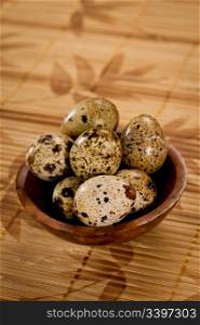 Delicate, beautiful Quail Eggs in a wood bowl on a bamboo mat. Shallow dof.