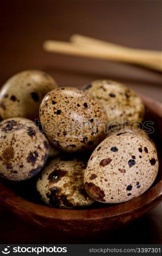 Delicate, beautiful Quail Eggs in a wood bowl with chopsticks in the background. Shallow depth of field.