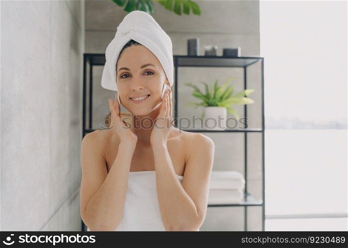 Delicate skin care and cosmetic applying. Girl is cleansing skin with face toner and cotton discs. Attractive european woman wrapped in towel after bathing. Young woman takes shower at home.. Delicate skin care and cosmetic applying. Girl is cleansing skin with face toner and cotton discs.
