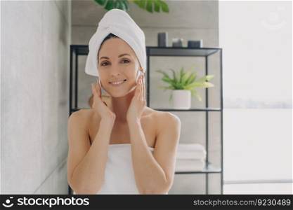 Delicate skin care and cosmetic applying. Girl is cleansing skin with face toner and cotton discs. Attractive european woman wrapped in towel after bathing. Young woman takes shower at home.. Delicate skin care and cosmetic applying. Girl is cleansing skin with face toner and cotton discs.