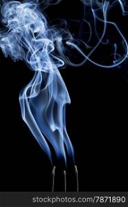 delicate smoke plume and swirls from burning three incense sticks