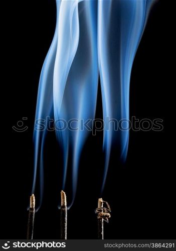 delicate smoke plumes from three burning incense sticks