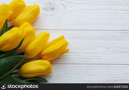 Delicate yellow tulips on white wooden background.  Top view,  space for text, border