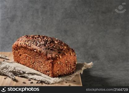 Delicious and healthy wheat - rye bread with seeds on sacking, close-up with selective focus. Fermented wholesome bread, healthy food. Loaf on gray background with space for text