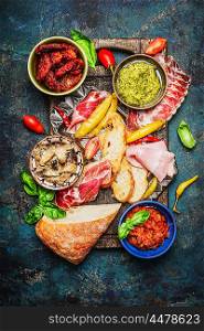 Delicious antipasti ingredients for bruschetta or crostini making on rustic background, top view. Italian food concept