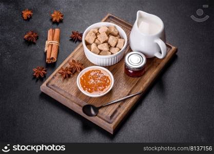 Delicious apricot jam, milk and sugar on a wooden cutting board against a dark concrete background. Delicious apricot jam, milk and sugar on a wooden cutting board
