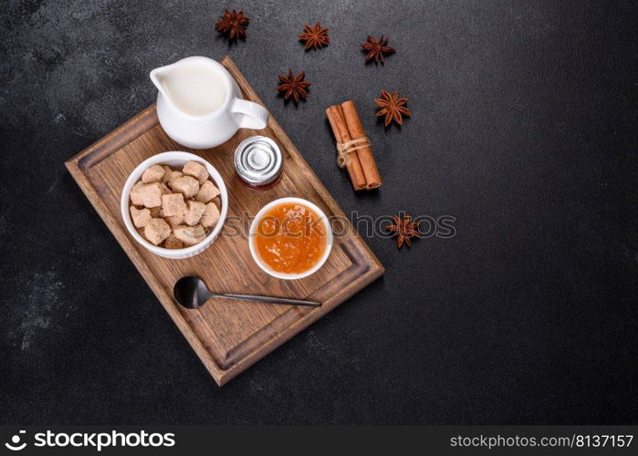 Delicious apricot jam, milk and sugar on a wooden cutting board against a dark concrete background. Delicious apricot jam, milk and sugar on a wooden cutting board