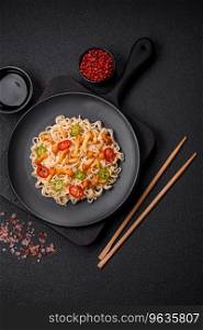 Delicious Asian cuisine dish with rice noodles, peppers, mushrooms and spices on a dark concrete background