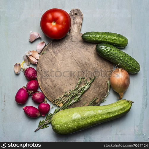 Delicious assortment of farm fresh vegetables around a round cutting board place for text,frame on wooden rustic background top view close up