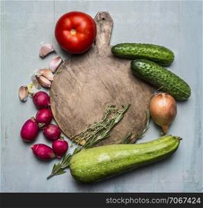 Delicious assortment of farm fresh vegetables around a round cutting board place for text,frame on wooden rustic background top view close up