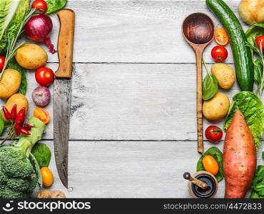 Delicious assortment of farm fresh vegetables with knife and spoon on white wooden background, top view. Vegetarian ingredients for cooking. Healthy cooking concept.