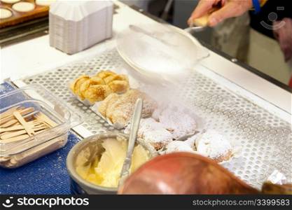 Delicious authentic Dutch food from The Netherlands called poffertjes, which are mini pancakes, being prepared for sale by adding butter and powdered confectioners sugar with a strainer.