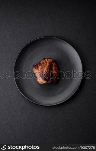 Delicious beef steak with salt, spices and herbs on a ceramic plate on a dark concrete background