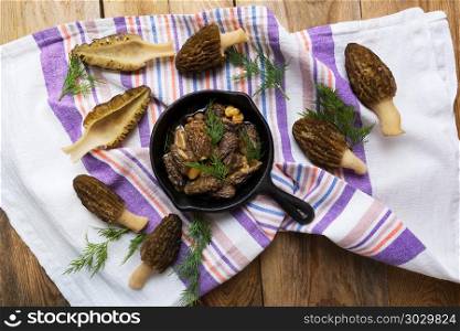 Delicious black morel mushrooms in skillet on rustic wooden table top view. Diet vegetarian food. . Black morel mushrooms in skillet