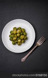 Delicious boi≤d Brussels sprouts on a ceramic plate on a dark concrete background. Ve≥tarian food