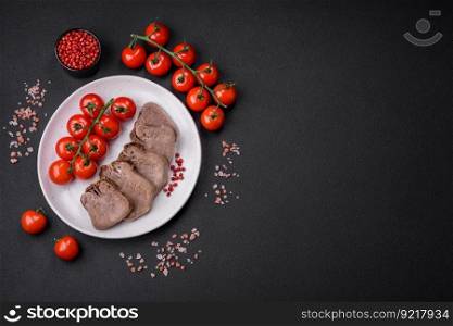 Delicious boiled beef tongue sliced with vegetables and spices on a dark concrete background