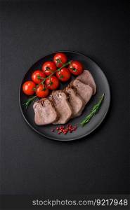 Delicious boiled beef tongue sliced with vegetables and spices on a dark concrete background