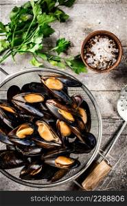 Delicious boiled mussels in a colander on the table. On a gray background. High quality photo. Delicious boiled mussels in a colander on the table.