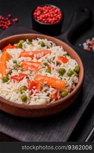 Delicious boiled rice with vegetables or risotto with salt, spices and herbs on a ceramic plate on a dark concrete background