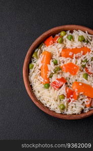 Delicious boiled rice with vegetables or risotto with salt, spices and herbs on a ceramic plate on a dark concrete background