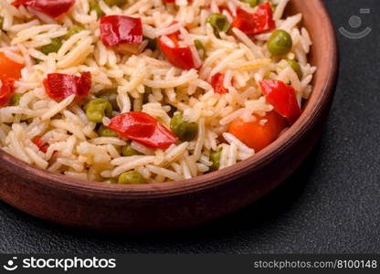 Delicious boiled rice with vegetables peppers, carrots, peas and asparagus beans with spices and herbs on a dark concrete background