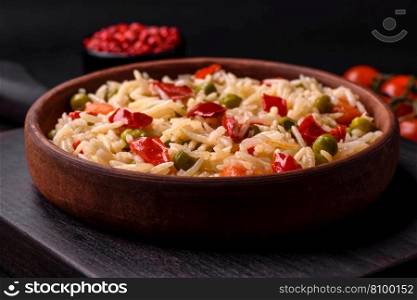 Delicious boiled rice with vegetables peppers, carrots, peas and asparagus beans with spices and herbs on a dark concrete background
