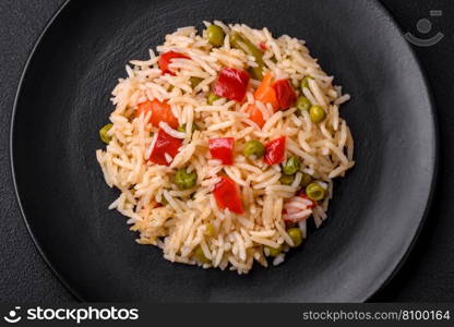 Delicious boiled rice with vegetables peppers, carrots, peas and asparagus beans with spices and herbs on a dark concrete background