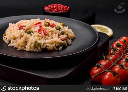 Delicious boiled rice with vegetables peppers, carrots, peas and asparagus beans with spices and herbs on a dark concrete background