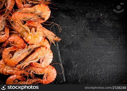 Delicious boiled shrimp on a stone board. On a black background. High quality photo. Delicious boiled shrimp on a stone board.
