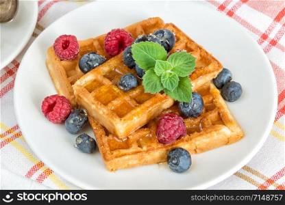 Delicious breakfast with sweet waffles, raspberries and blueberries on a checkered napkin