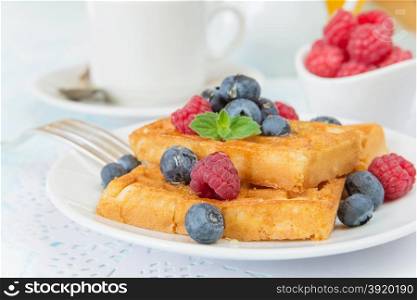 Delicious breakfast with sweet waffles, raspberries, blueberries and a cup of coffee