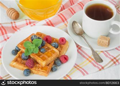 Delicious breakfast with sweet waffles, raspberries, blueberries and a cup of coffee on a checkered napkin