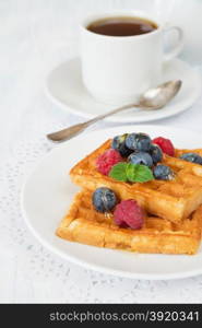 Delicious breakfast with sweet waffles, raspberries, blueberries and a cup of coffee, vertical photo