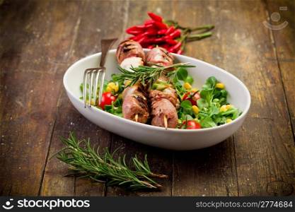 delicious broiled meat skewers on wooden table with salad