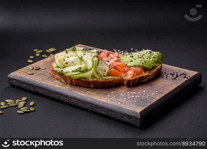 Delicious brown bread toast with salmon, avocado, cucumber and sesame seeds on a textured concrete background