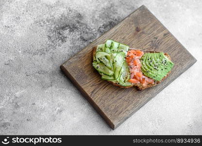 Delicious brown bread toast with salmon, avocado, cucumber and sesame seeds on a textured concrete background