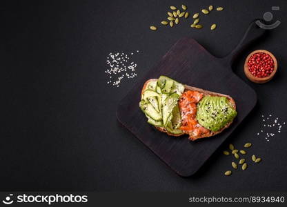 Delicious brown bread toast with salmon, avocado, cucumber and sesame seeds on a textured concrete background