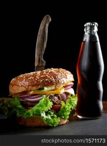 delicious burger with fried beef cutlet and onions. crispy white wheat flour bun with sesame seeds. Fast food on a wooden board, behind a bottle with a drink